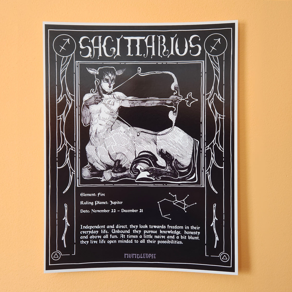 A black and white art print featuring a detailed illustration of a Sagittarius zodiac sign. The print includes astrological details such as the ruling planet Jupiter, dates from November 22 to December 21, and a short description of the Sagittarius personality, all framed by an ornate border. Zodiac index. On wall